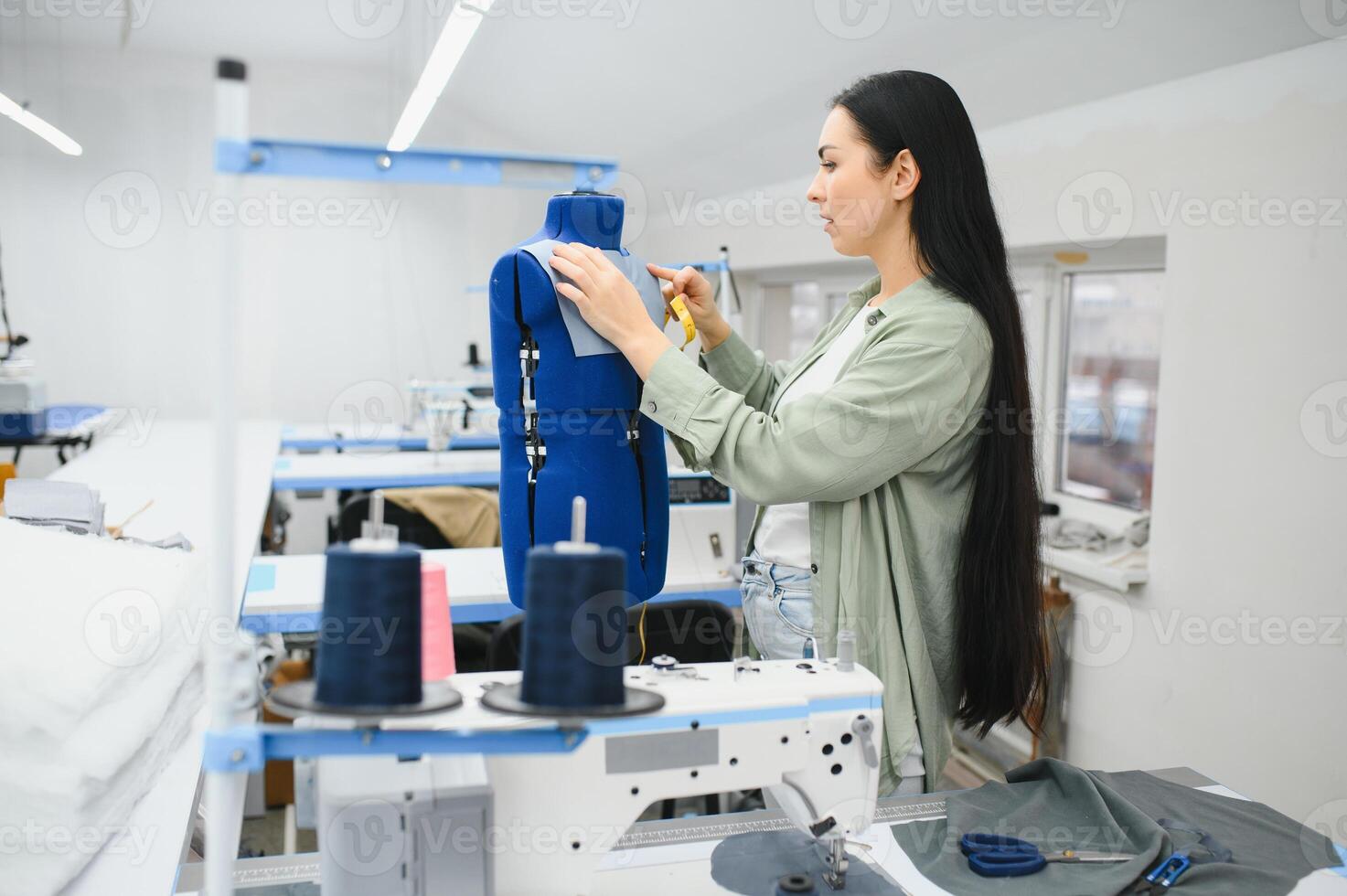feliz fêmea costureira trabalhando com de costura máquina às têxtil fábrica. foto