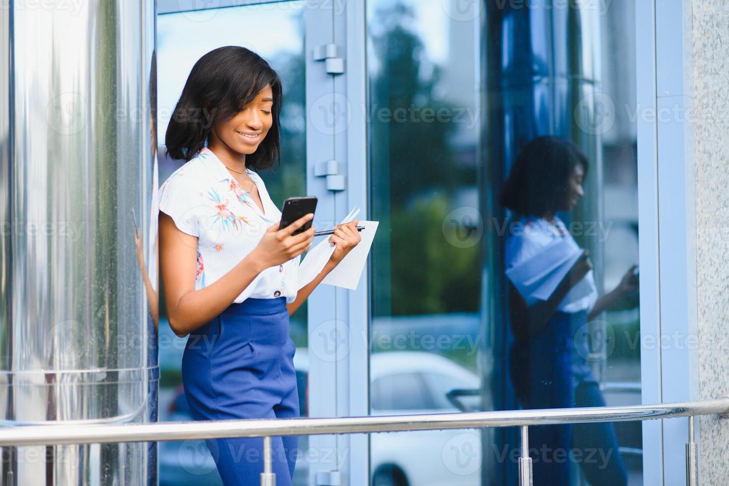 lindo africano americano menina em pé em rua com celular e café dentro mãos enquanto alegremente olhando aparte. retrato do africano americano senhora em rua. foto