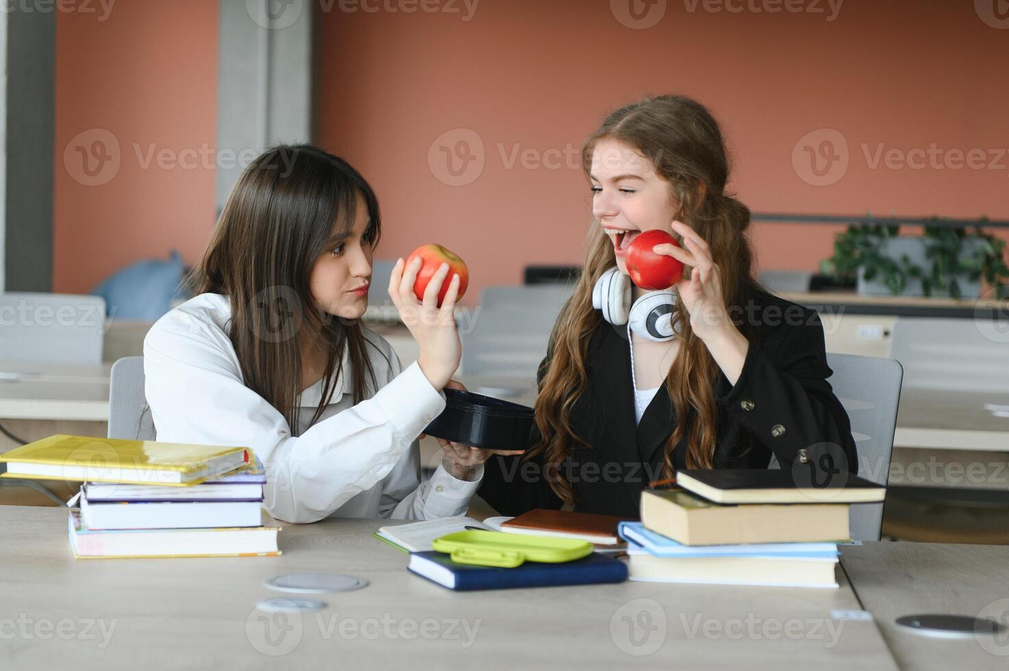 dois feliz sorridente fêmea alunos estão sentado e comendo maçãs, estudando e preparando para exames. foto