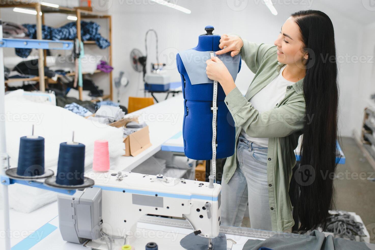 feliz fêmea costureira trabalhando com de costura máquina às têxtil fábrica. foto