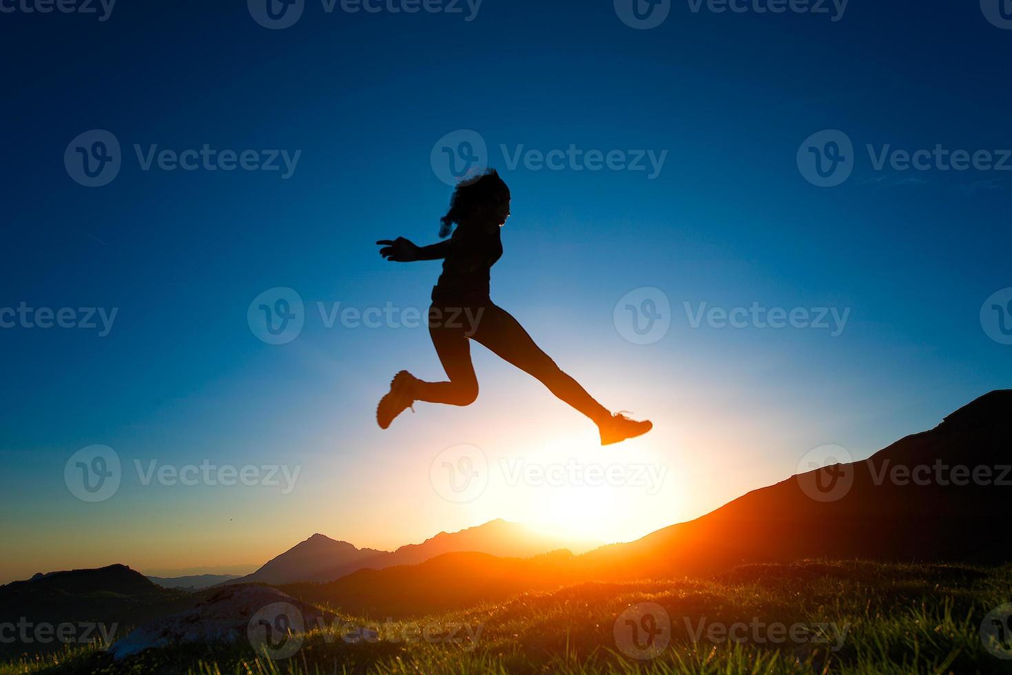 garota pula durante um pôr do sol nas montanhas foto