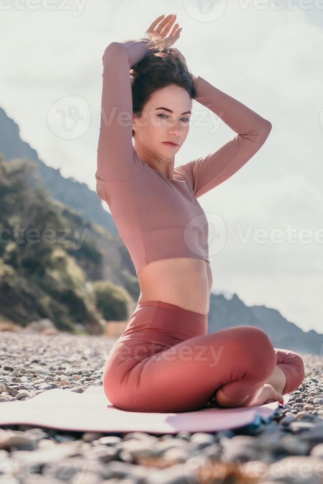 meio envelhecido bem olhando mulher com Preto cabelo, ginástica instrutor dentro perneiras e tops fazendo alongamento e pilates em ioga esteira perto a mar. fêmea ginástica ioga rotina conceito. saudável estilo de vida foto