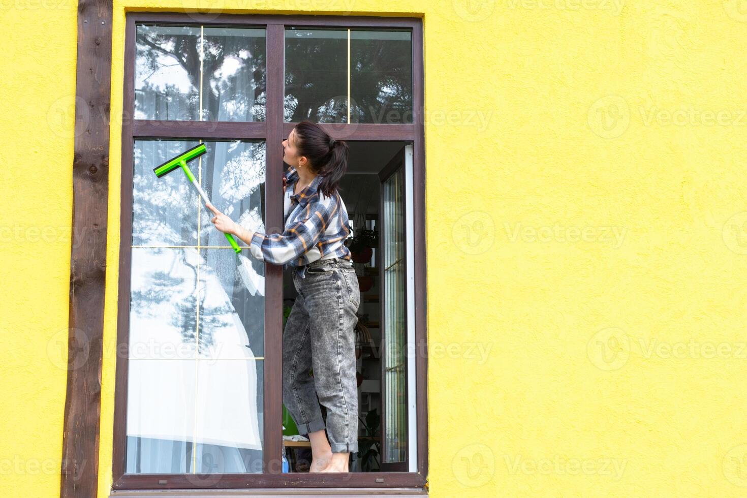 uma mulher manualmente lavagens a janela do a casa com uma trapo com uma spray limpador e uma esfregão fora. segurança às altura, restaurando ordem e limpeza dentro a primavera, limpeza serviço foto