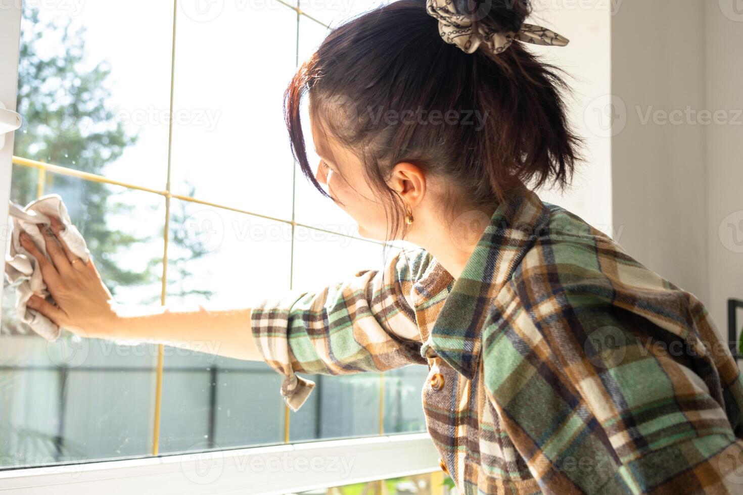 mulher manualmente lavagens a janela do a casa com uma trapo com spray limpador e esfregão dentro a interior com branco cortinas. restaurando ordem e limpeza dentro a primavera, limpeza servise foto