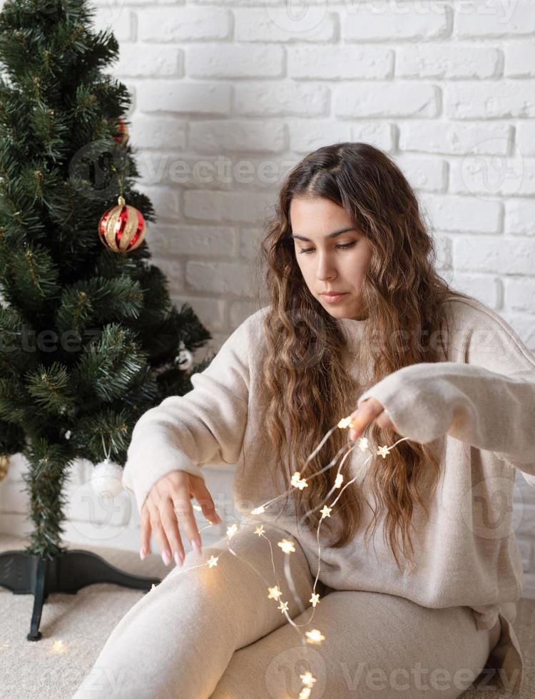 jovem mulher atraente decorando a árvore de natal com luzes de fada foto