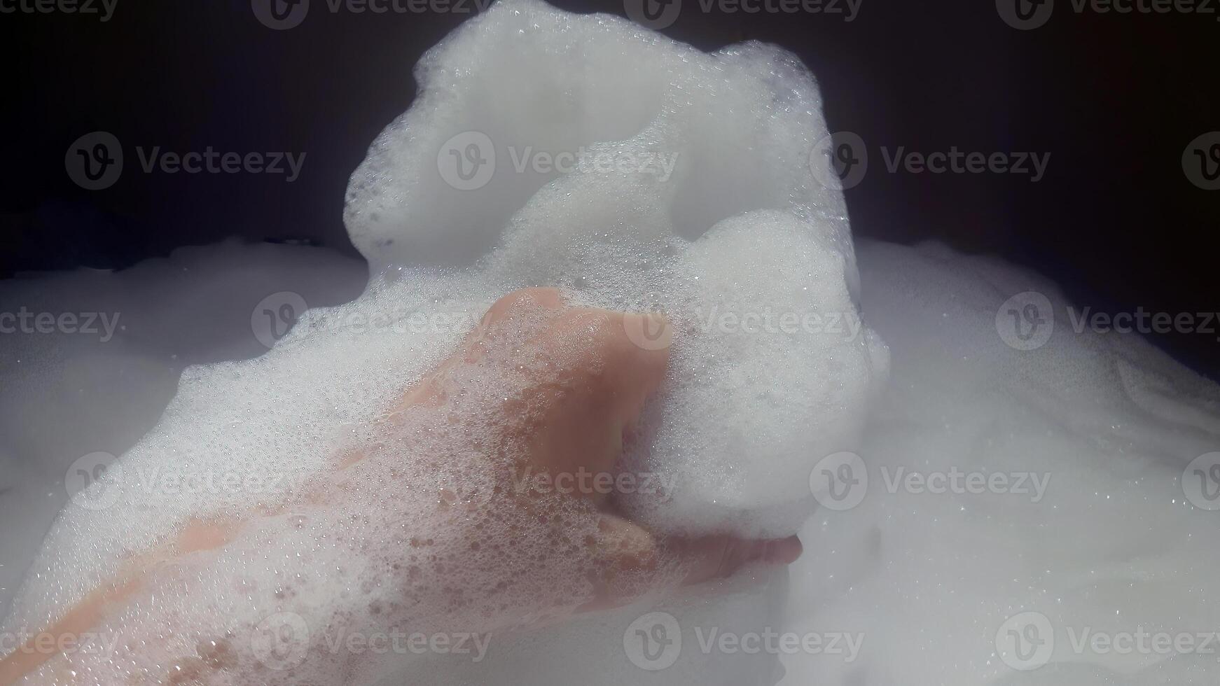 uma fêmea mão jogando Sabonete bolhas espuma dentro a banheira, spa, casa relaxar, tomando banho dentro suave iluminação, banheiro, feliz refrescar tempo, espuma banho, cuidados com a pele, o negócio conceito foto