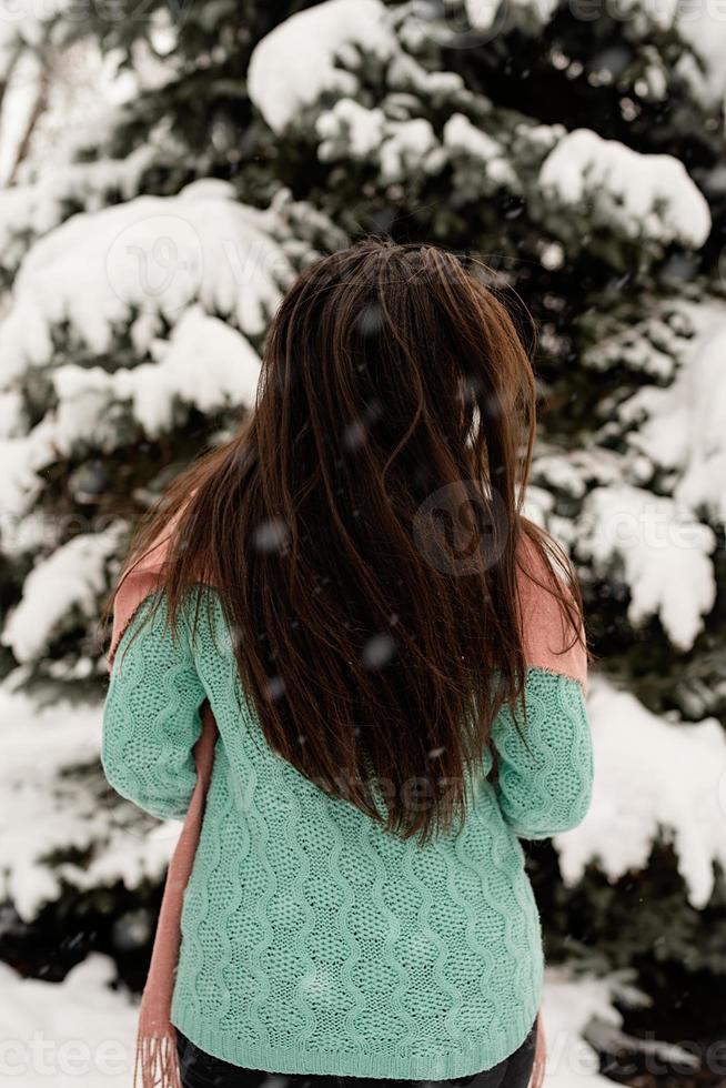 vista traseira de uma mulher morena com roupas de inverno rosa, em pé ao ar livre em um dia de neve perto da árvore de Natal foto