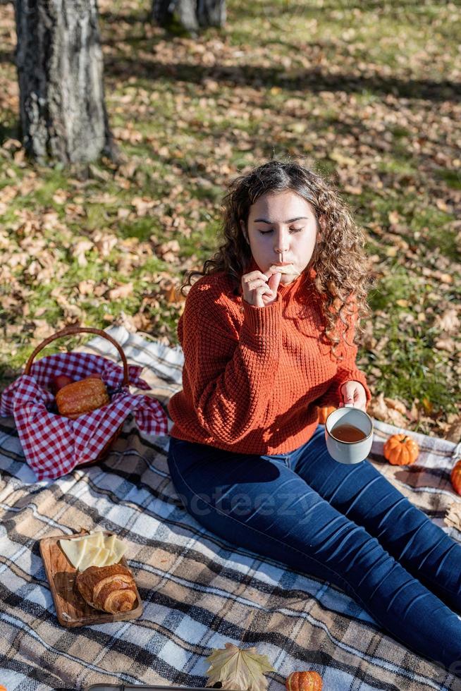 Mulher bonita em um suéter vermelho em um piquenique em uma floresta de outono foto