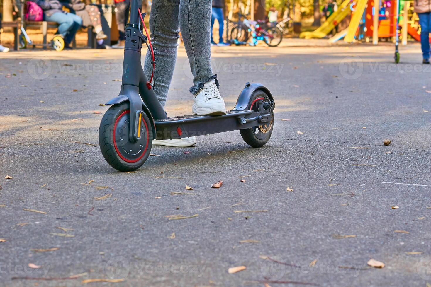 fêmea pernas dentro cinzento jeans em a elétrico lambreta dentro uma público parque foto