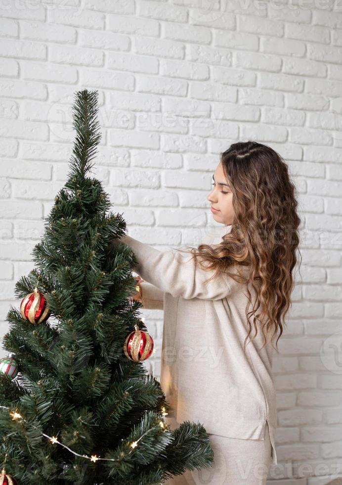 jovem mulher atraente decorando a árvore de natal com luzes de fada foto