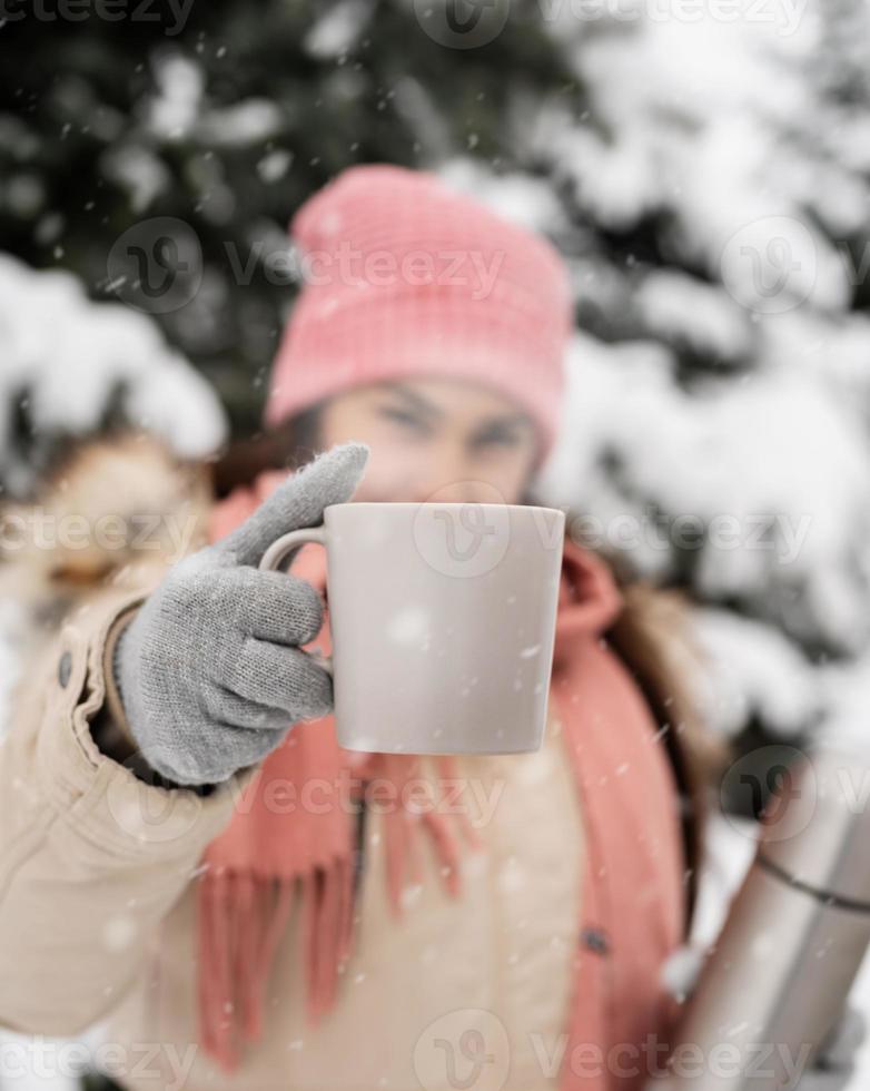 closeup de mulher com roupas de inverno segurando uma caneca com chá quente ou café ao ar livre em dia de neve foto