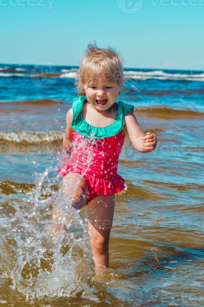 jovem feliz criança menina do europeu aparência era do 4 tendo Diversão dentro água em a de praia e salpicos, tropical verão vocações, feriados.a criança goza a mar.vertical foto. foto