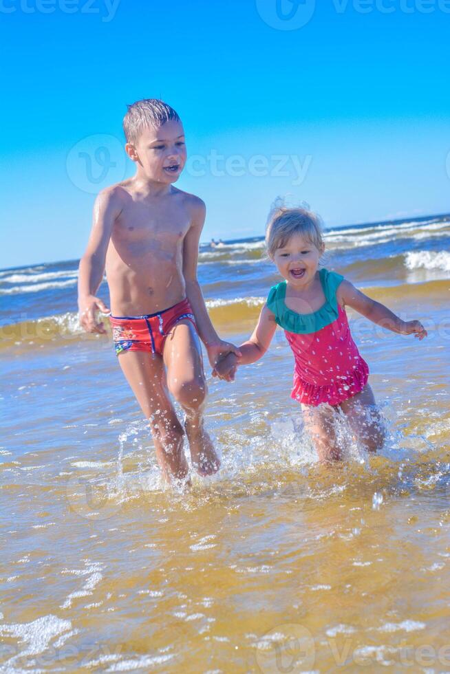 jovem feliz criança menina e Garoto do europeu aparência tendo Diversão dentro água e corrida em praia, e salpicos, tropical verão vocações, feriados.a criança goza a mar.família feriados conceito.vertical foto. foto