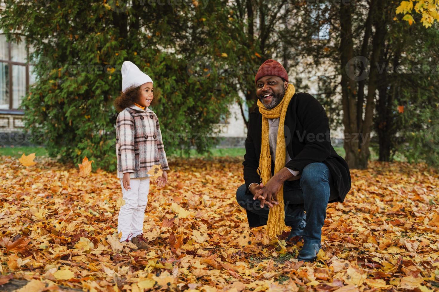 avô e neta negros se divertindo com folhas caídas no parque de outono foto