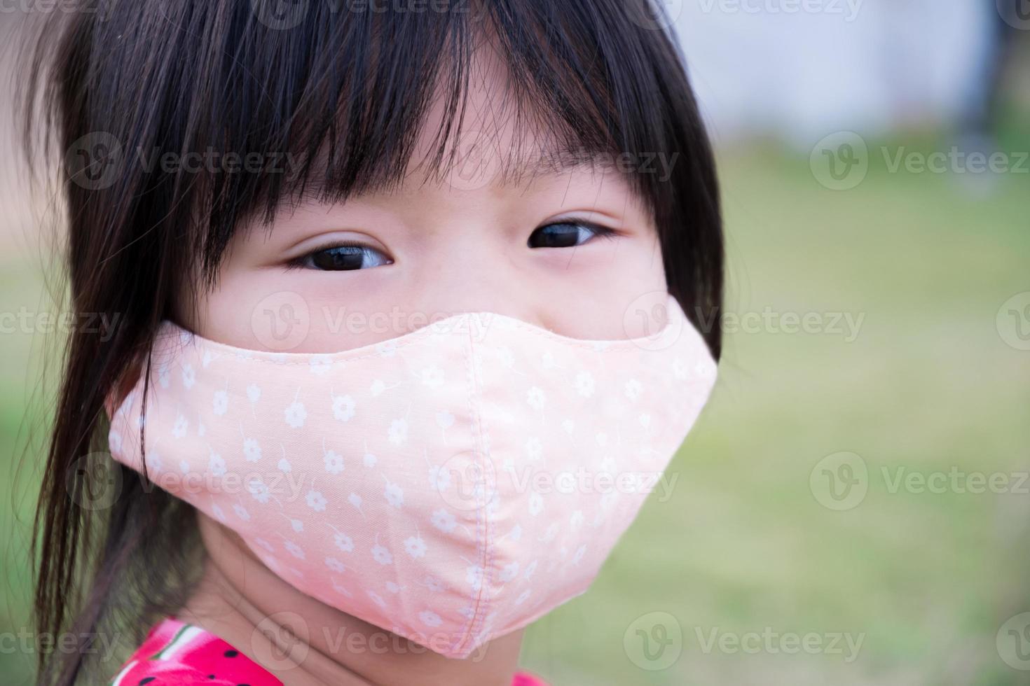 criança usando máscara facial de pano para prevenir a disseminação da doença do coronavírus covid 19. menina rosto do close up. no parque público. criança de 4-5 anos. foto