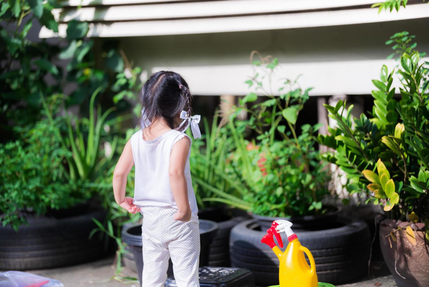 As costas da menina asiática ajudam a família nos trabalhos domésticos. menina se prepara para regar as plantas com um regador amarelo-vermelho colocado ao seu lado. conceito de treinar crianças para assumir responsabilidades. foto