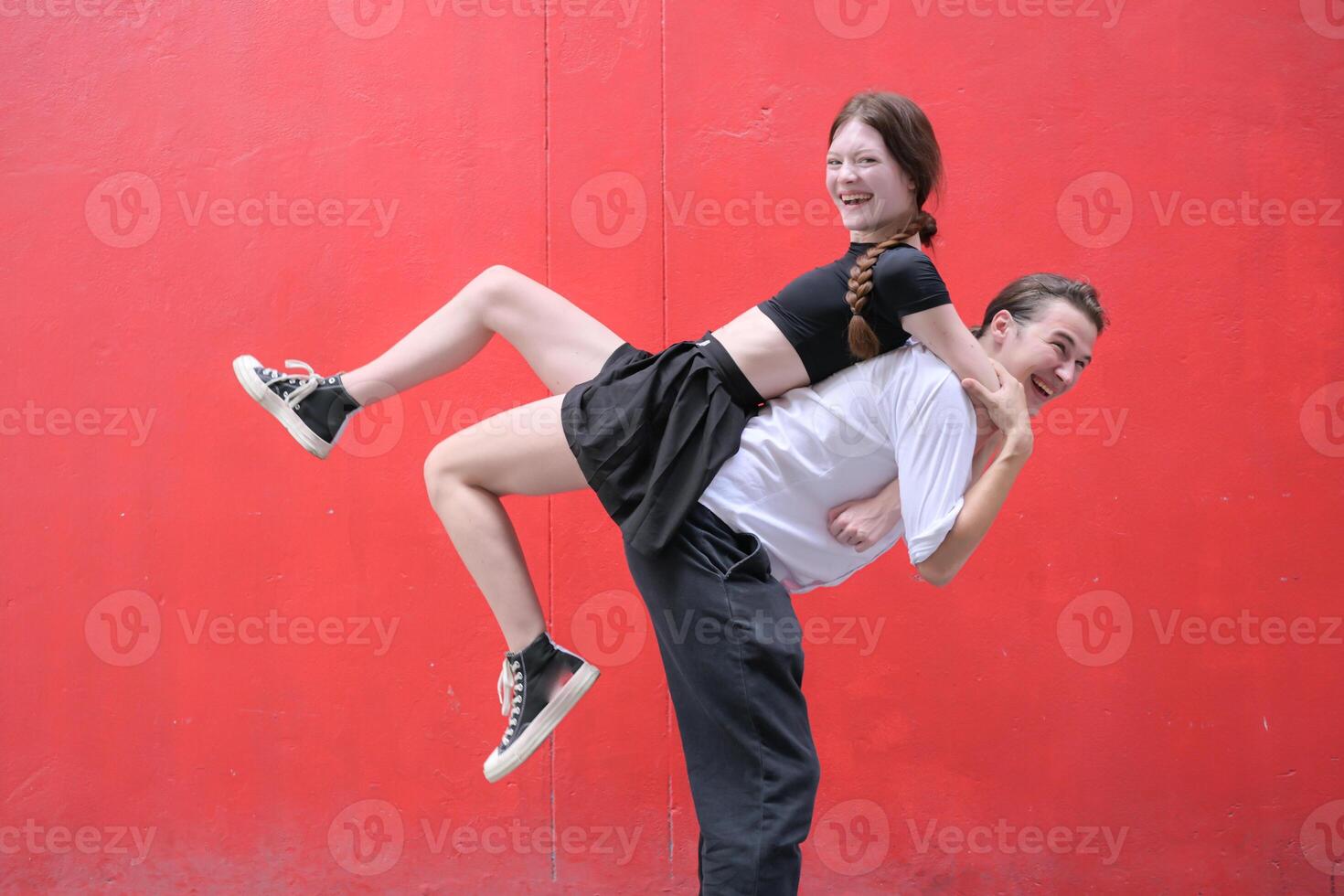 uma casal é desfrutando uma verão período de férias dentro a vermelho parede fundo, alegremente mostrando seus amor para cada outro. foto