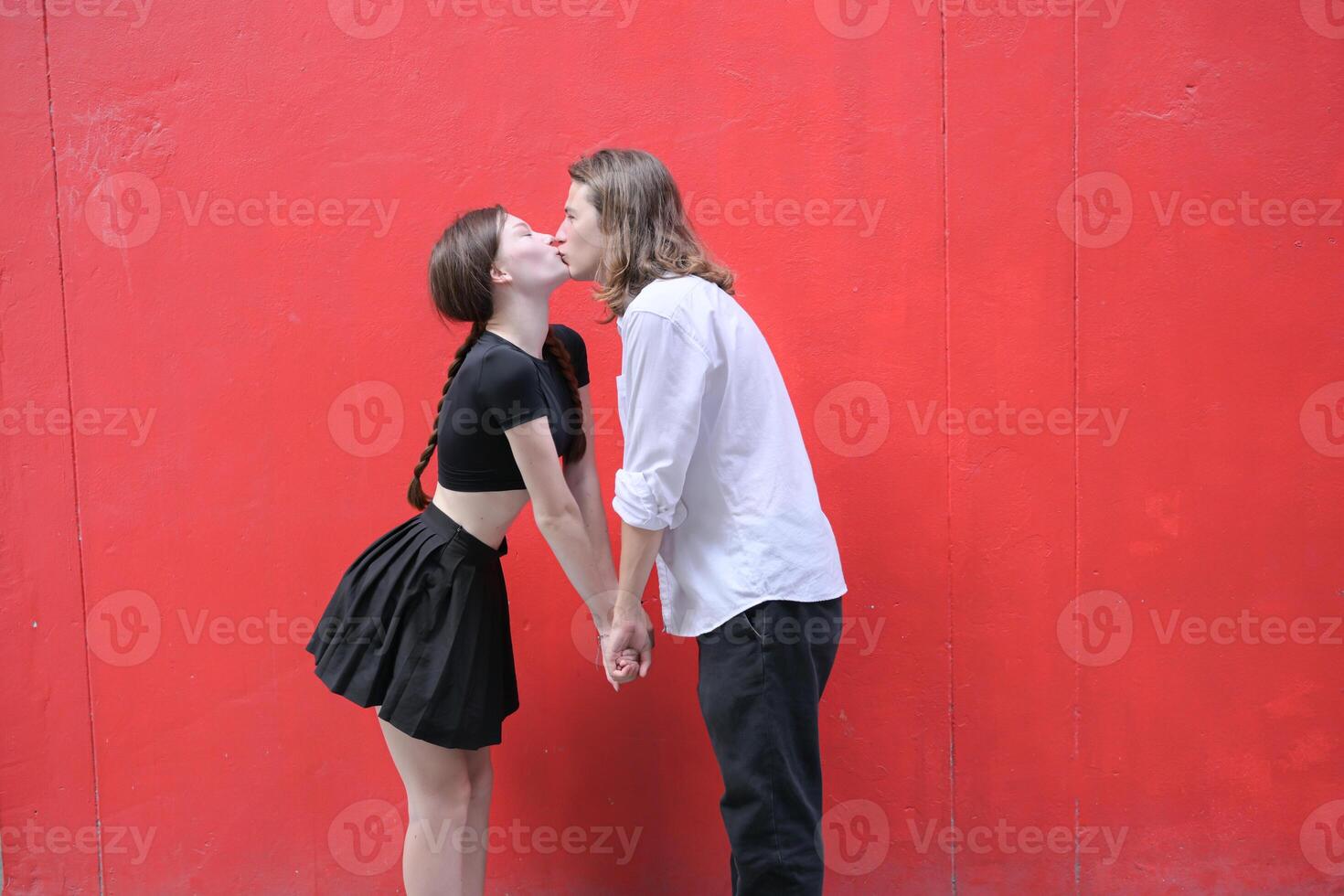 uma casal é desfrutando uma verão período de férias dentro a vermelho parede fundo, alegremente mostrando seus amor para cada outro. foto