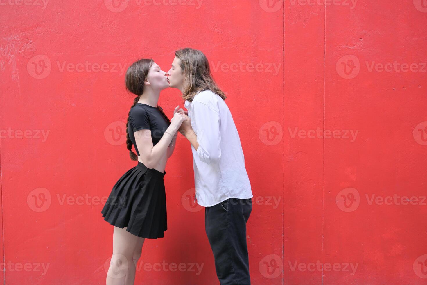 uma casal é desfrutando uma verão período de férias dentro a vermelho parede fundo, alegremente mostrando seus amor para cada outro. foto