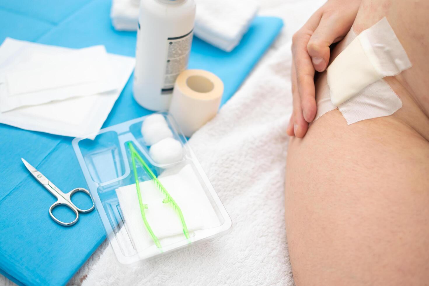 fechar acima Visão do mão tocante ferida com gaze em quadril e ajuda kit utensílios foto