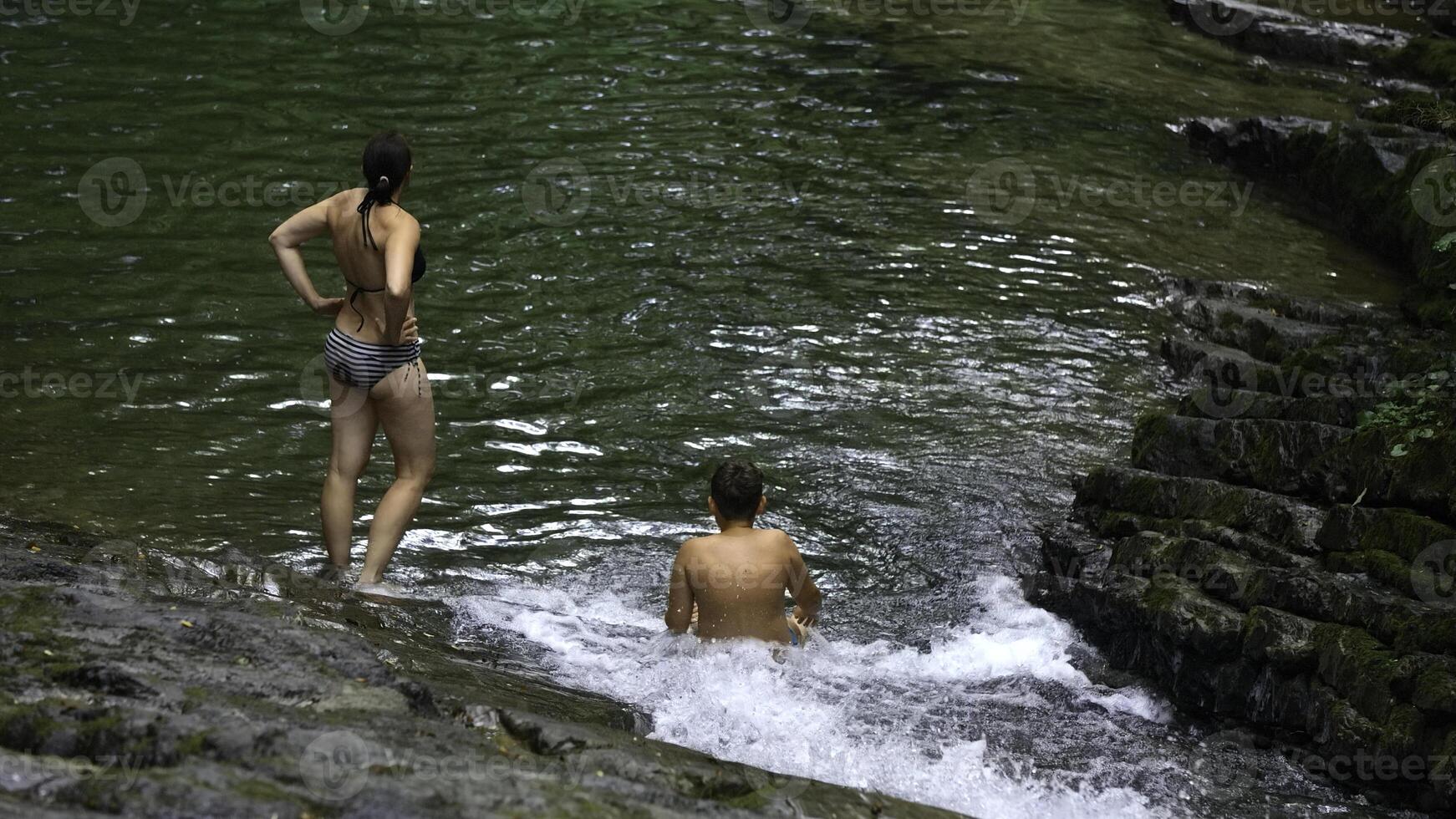 mulher e Adolescência Garoto tomando banho dentro espirrando cascata dentro tropical floresta. criativo. feliz família desfrutando fresco água a partir de fluindo cascata dentro selva. foto