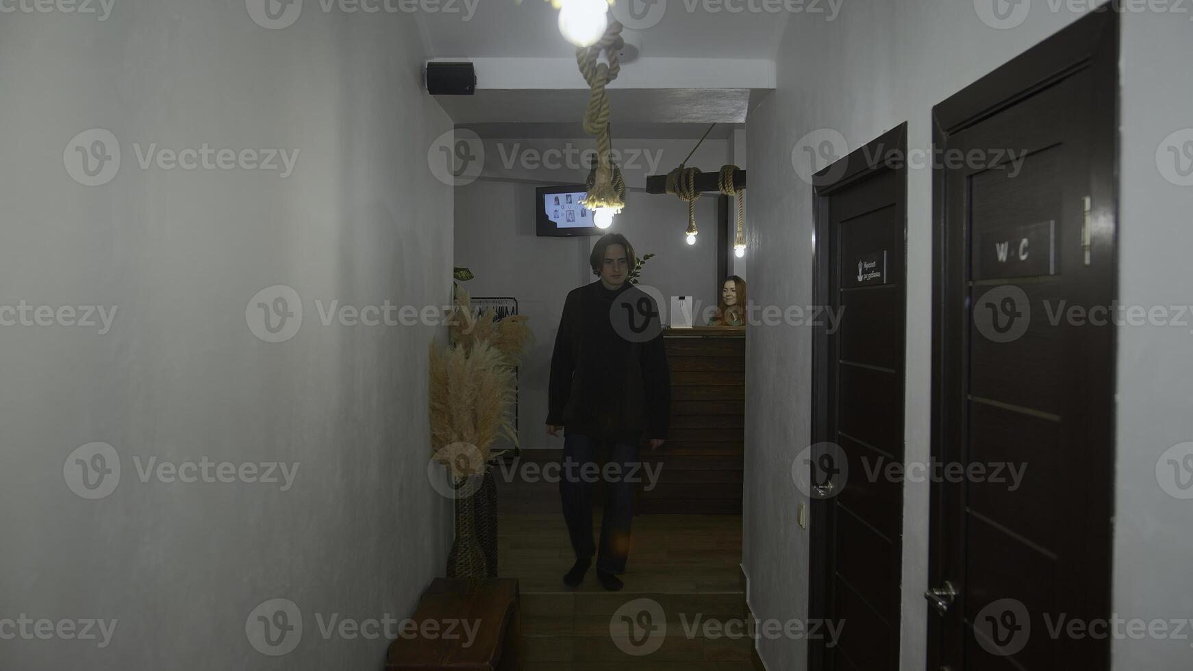 jovem homem caminhando ao longo a hotel corredor e entrando a banheiro. meios de comunicação. bonito homem paquera e piscando. foto