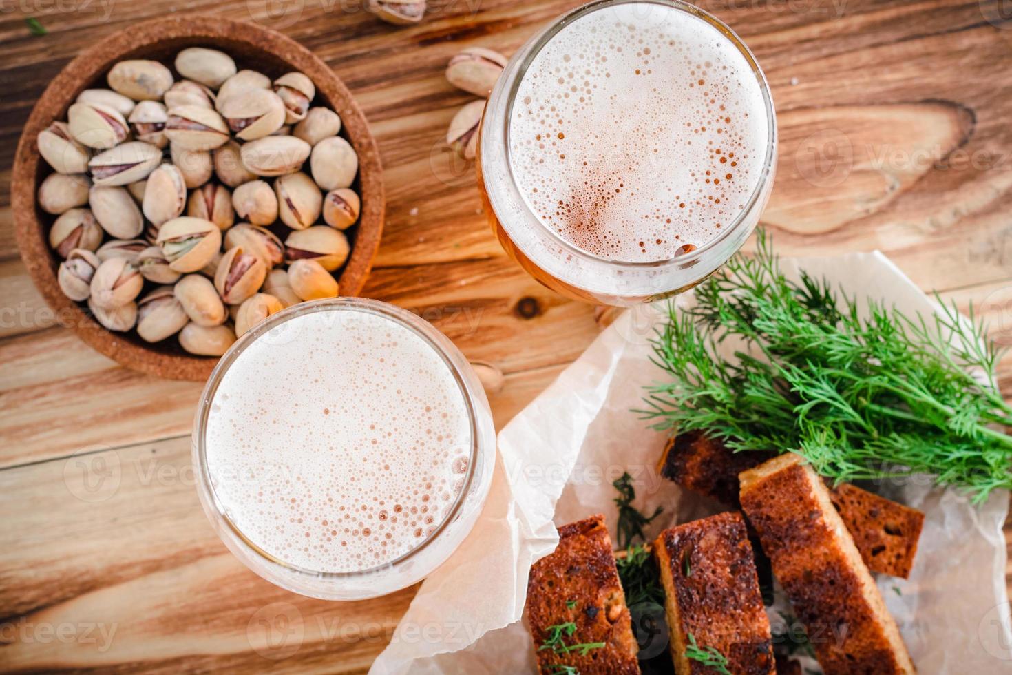 dois copos de cerveja, torradas torradas com crosta, endro e pistache sobre uma mesa de madeira. foco seletivo na espuma foto