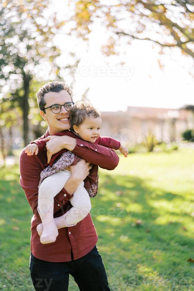 sorridente Papai abraços pequeno menina segurando dela dentro braços dentro parque foto