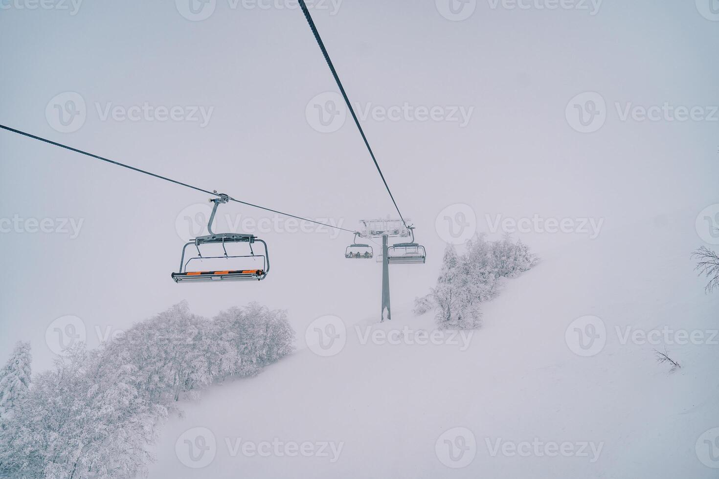 quatro lugares teleférico sobe acima uma coberto de neve floresta ao longo uma enevoado lado da montanha foto