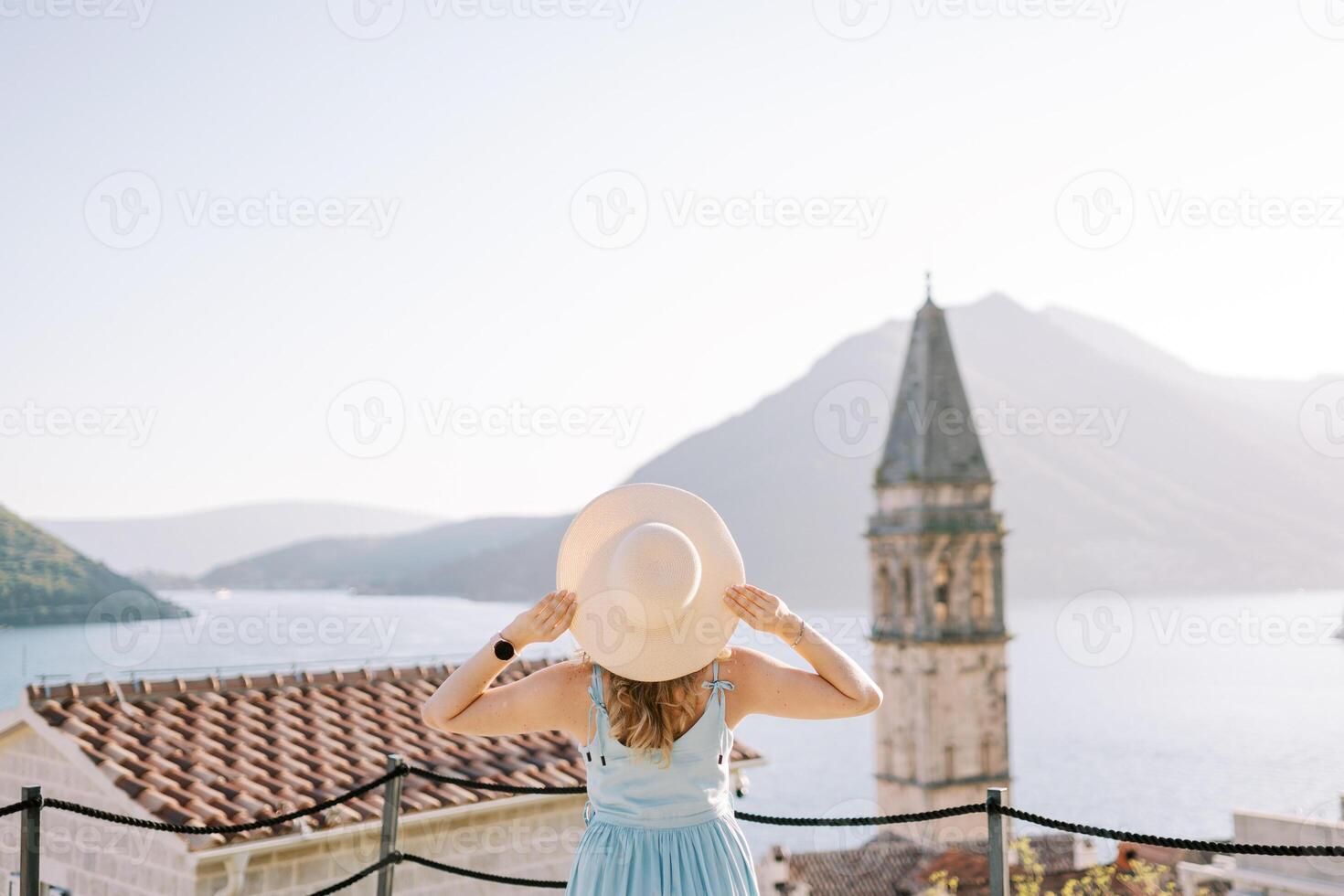 menina carrinhos em a observação área coberta perto a Sino torre, segurando dela chapéu com dela mãos. perast, Montenegro. costas Visão foto