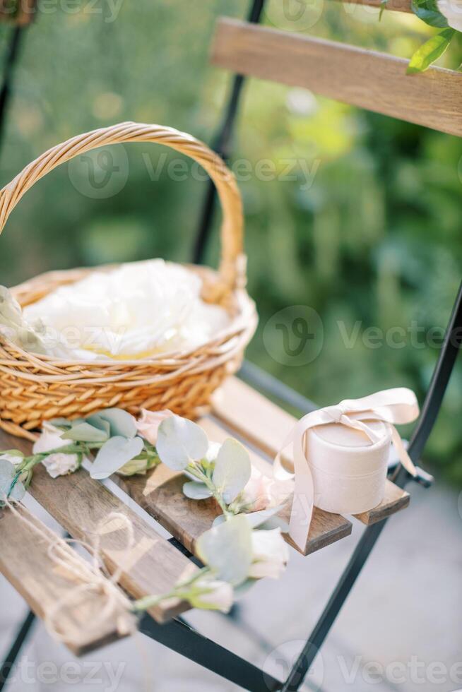 guirlanda, uma vime cesta com flores e uma caixa com joalheria carrinhos em uma de madeira cadeira dentro a jardim foto