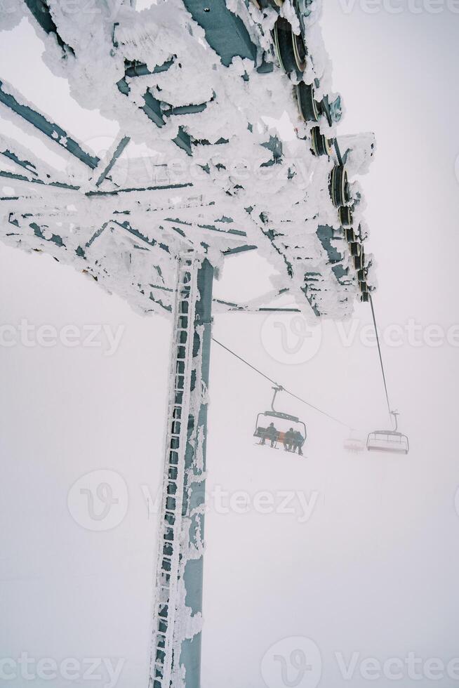 coberto de neve pilar do uma quatro lugares teleférico com comovente cadeiras foto