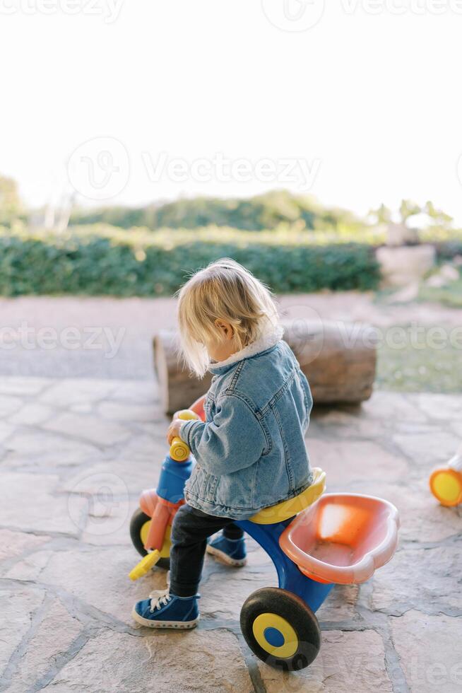 pequeno menina senta em uma triciclo e parece às a direção roda foto