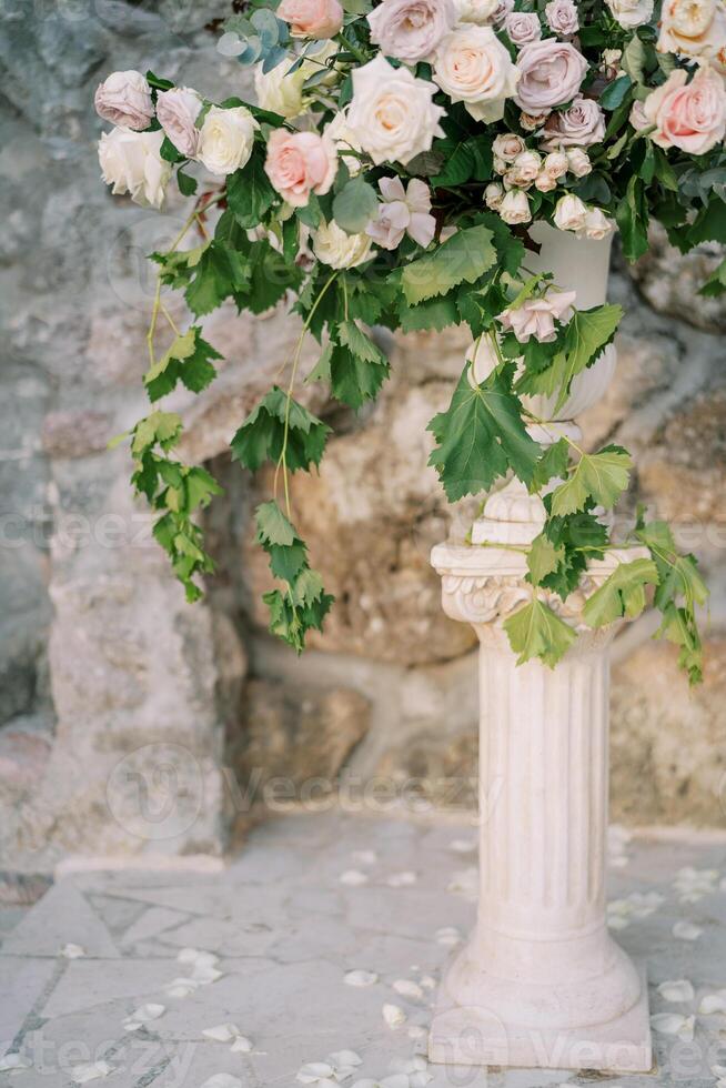 exuberante ramalhete do flores carrinhos dentro uma vaso em uma pedestal perto uma pedra parede dentro a jardim foto