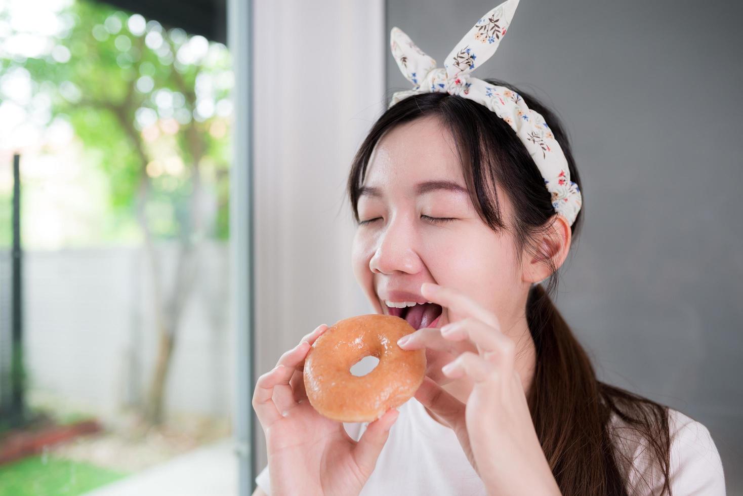 mulher jovem asiática feliz é deliciosamente mordendo uma rosquinha doce. foto
