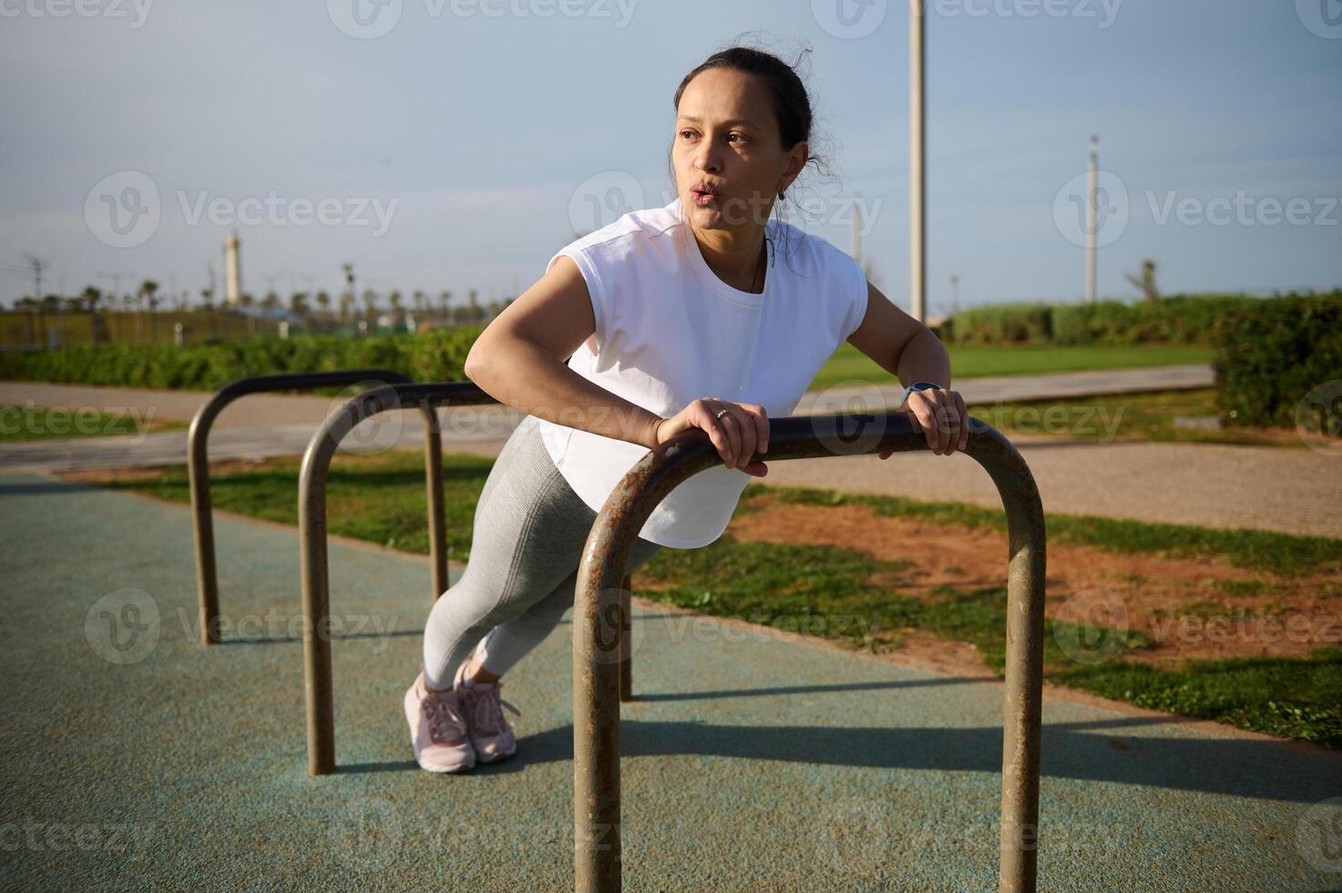 jovem desportivo mulher exercício ao ar livre, fazendo braços exercícios, empurrando acima em Cruz Barra foto