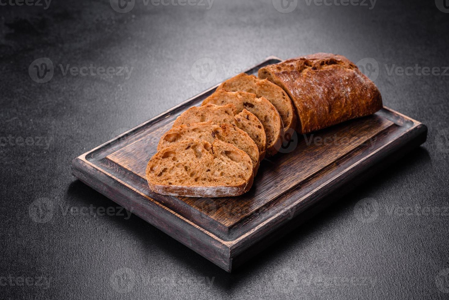 delicioso pão preto fresco fatiado com fatias em um fundo escuro de concreto foto