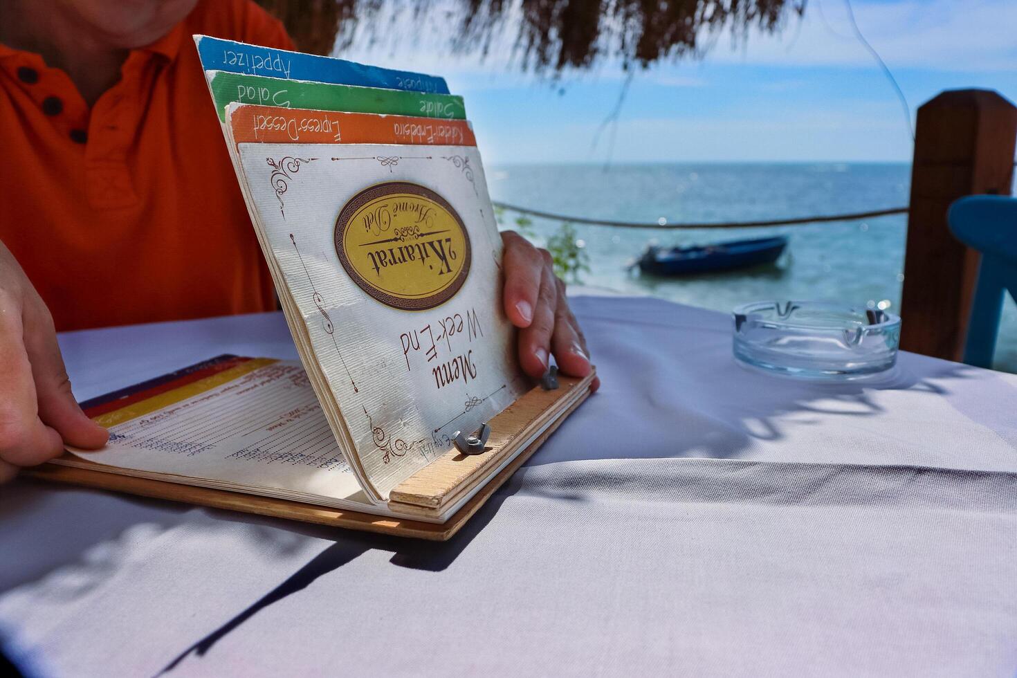 dura, Albânia - setembro 3º 2022. restaurante 2 kitarrat arome deti. homem segurando e lendo a cardápio cartão, escolhendo a refeição. lindo restaurante em adriático mar de praia em uma ensolarado dia. foto