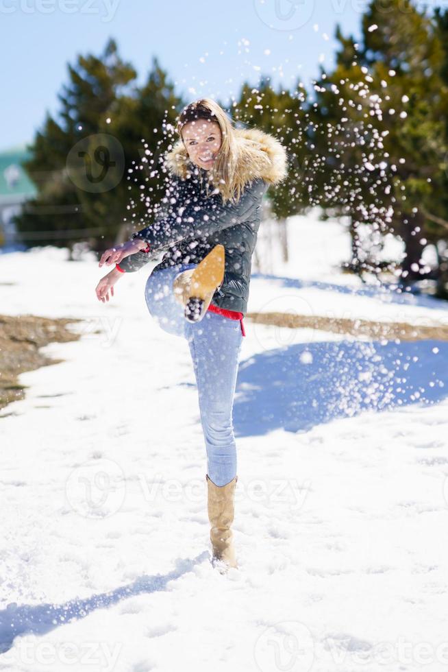 jovem mulher feliz chutando neve em uma floresta coberta de neve nas montanhas foto