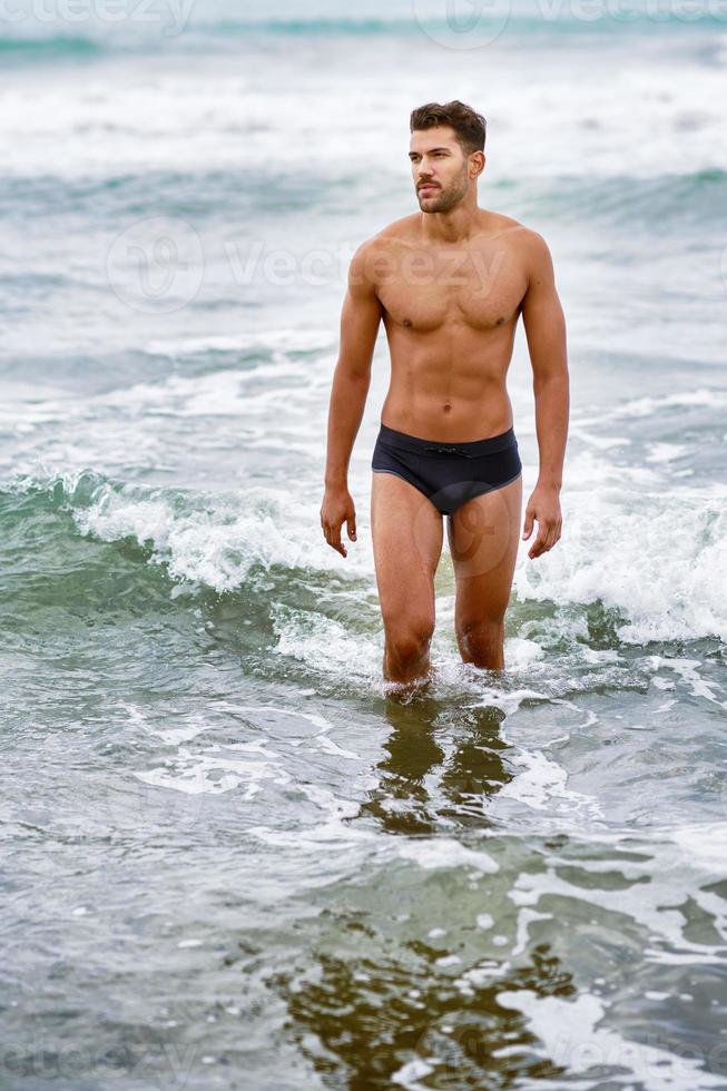 belo homem musculoso tomando banho na praia foto