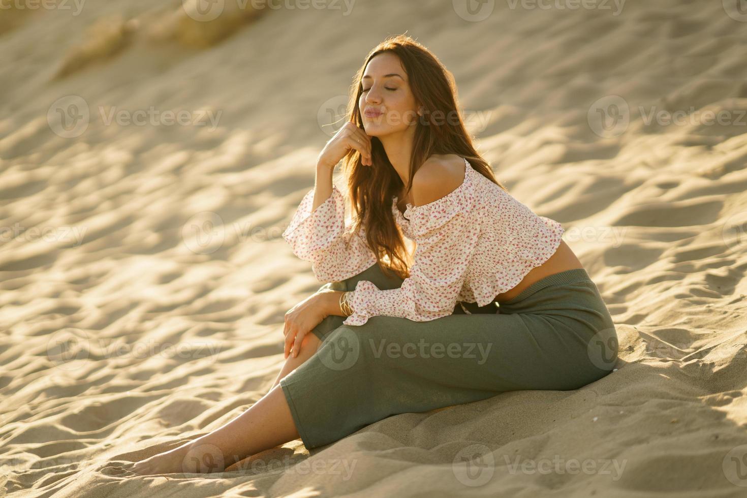 jovem sentada na areia da praia com os olhos fechados foto