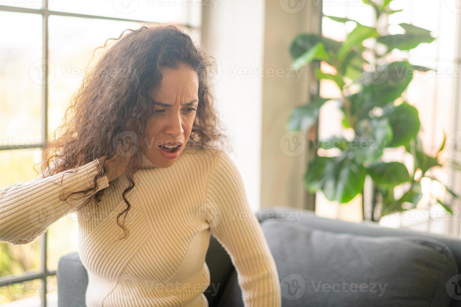 mulher latina sentada no sofá com sensação de dor no pescoço foto