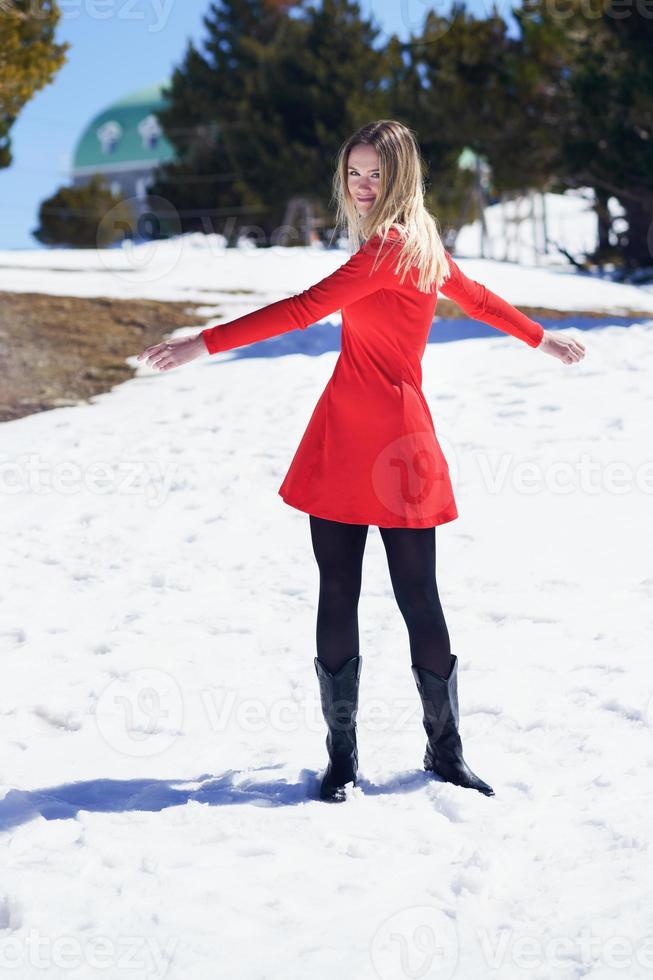 mulher usando um vestido vermelho e meias pretas, abrindo os braços de felicidade nas montanhas nevadas. foto