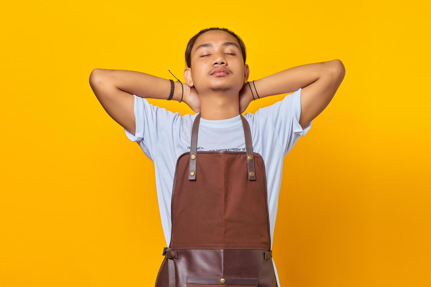 retrato de jovem asiático calmo e relaxado, aliviando o estresse, fechando os olhos e sorrindo pacificamente isolado no fundo amarelo foto