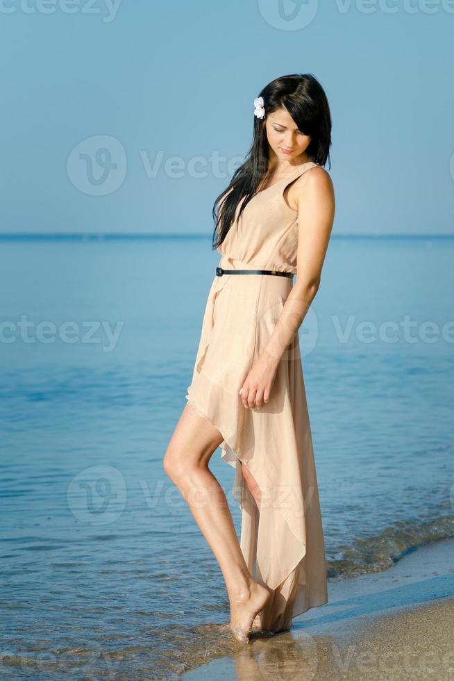 garota com cabelo preto em um vestido bege na costa do oceano foto