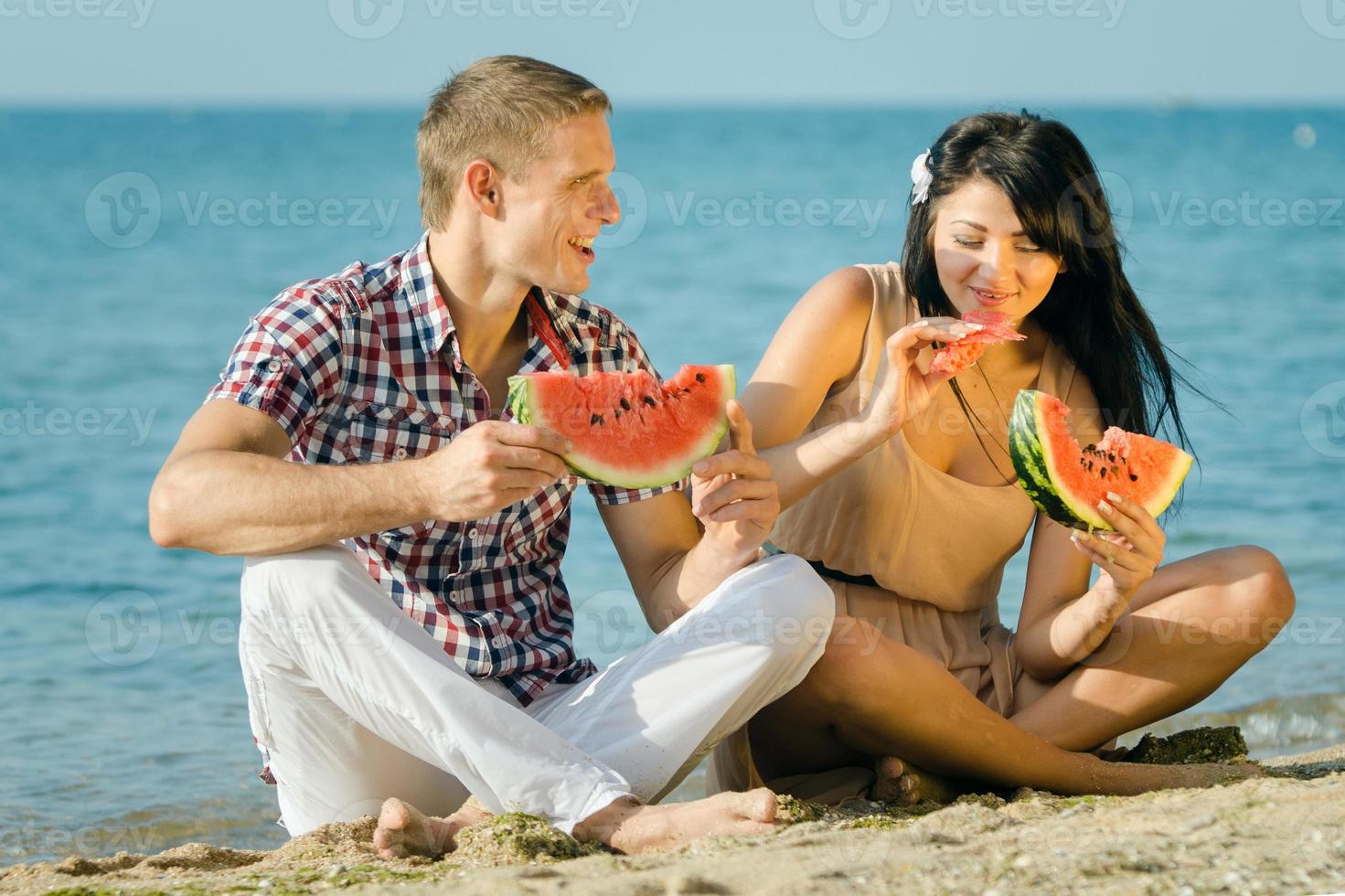 cara e uma garota na praia comendo uma melancia madura foto