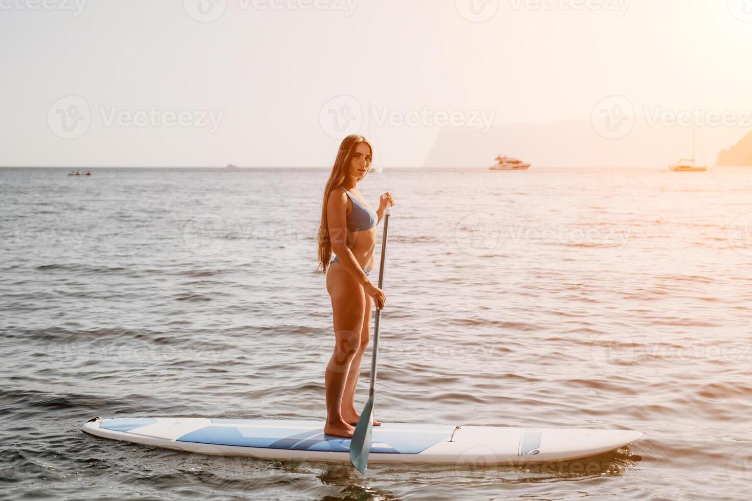 mulher mar e aí. fechar acima retrato do feliz jovem caucasiano mulher com grandes cabelo olhando às Câmera e sorridente. fofa mulher retrato dentro uma azul bikini posando em sup borda dentro a mar foto