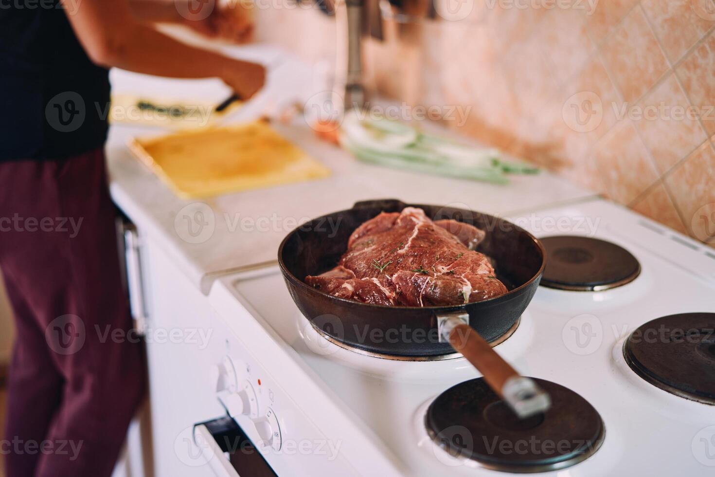cru assado carne é cozido dentro uma fritar panela em uma fogão perto uma cozinhar corte legumes foto