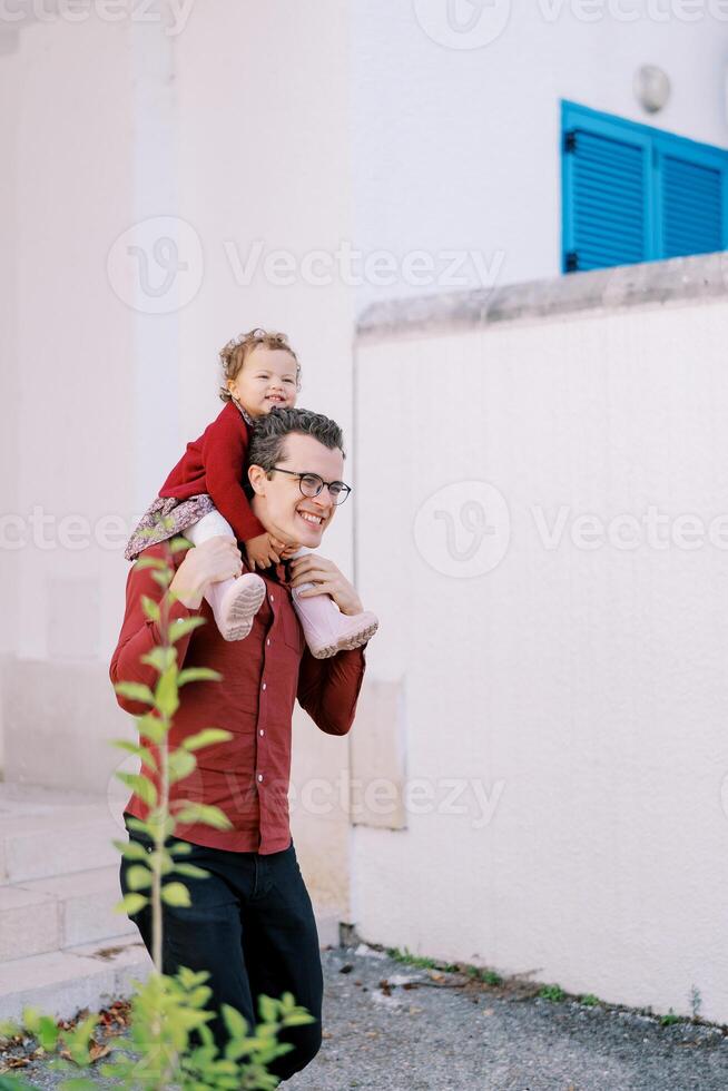 sorridente Papai carrega em dele ombros uma pequeno menina abraçando dele pescoço foto