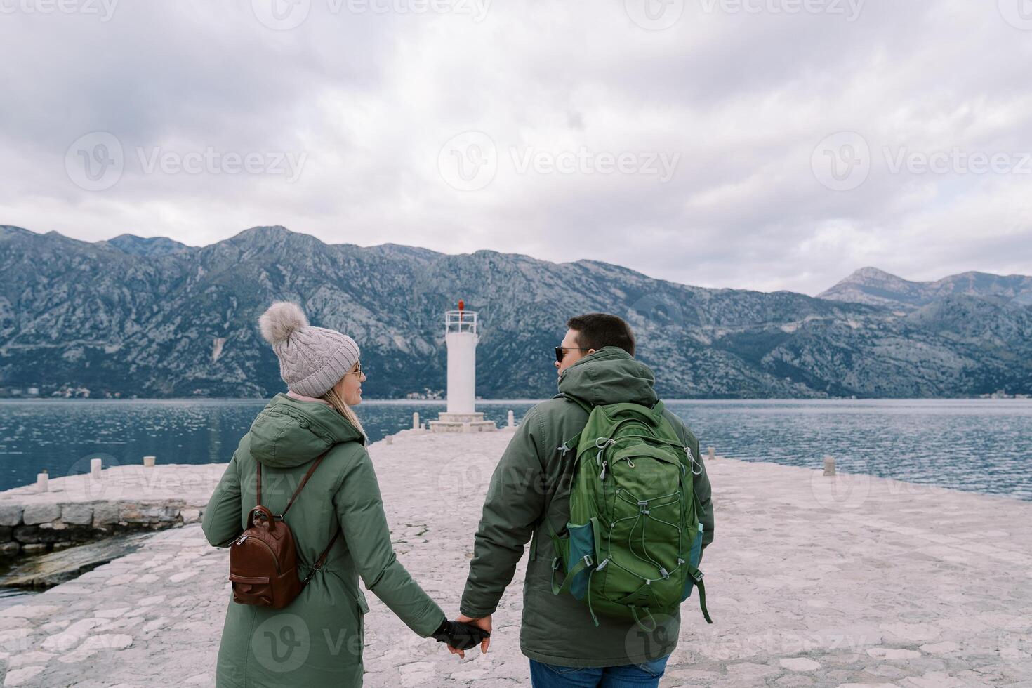 Viajantes andar ao longo a cais para a farol segurando mãos. costas Visão foto